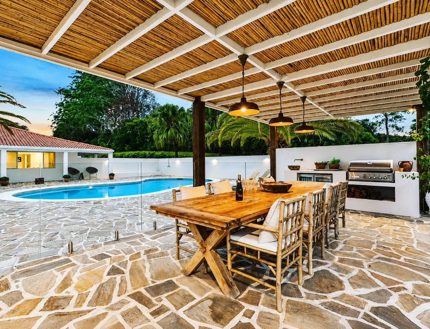 Clunes pool pavilion renovation in the Byron hinterland — bamboo-roofed outdoor dining pavilion with built-in barbecue kitchen, flagstone paving and glass-fenced pool